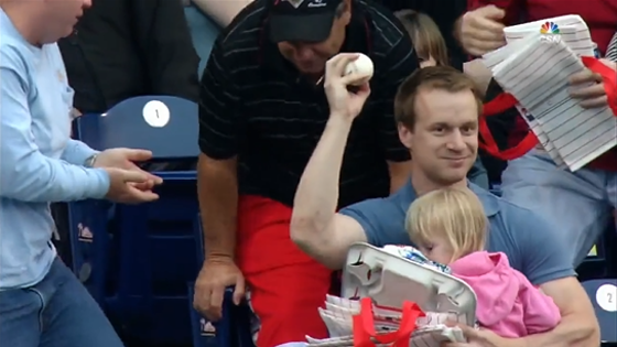 En tenant sa fille et sa nourriture dans les bras, il attrape une balle de baseball