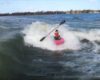 Un kayakiste prend une vague de sillage entre 2 bateaux sur un lac