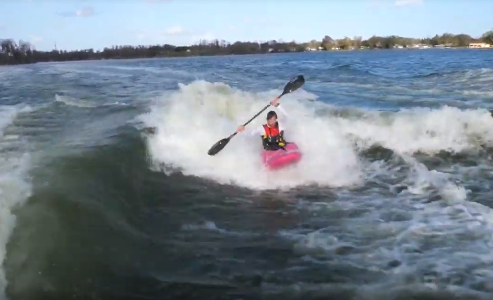 Un kayakiste prend une vague de sillage entre 2 bateaux sur un lac